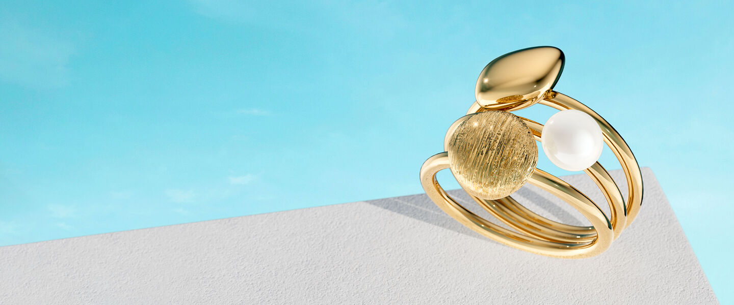 A Birks Pebble yellow gold and pearl ring on a blue background.